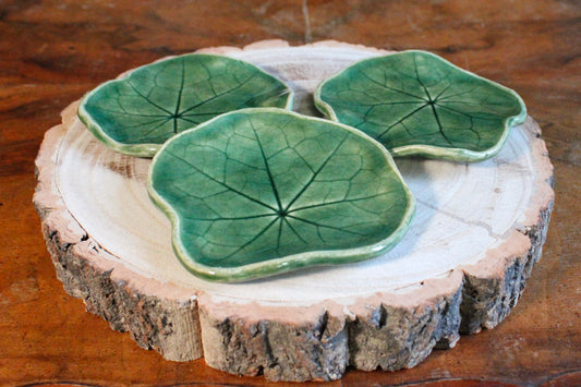 Three green ceramic leaf-shaped shallow dishes on a log slice.