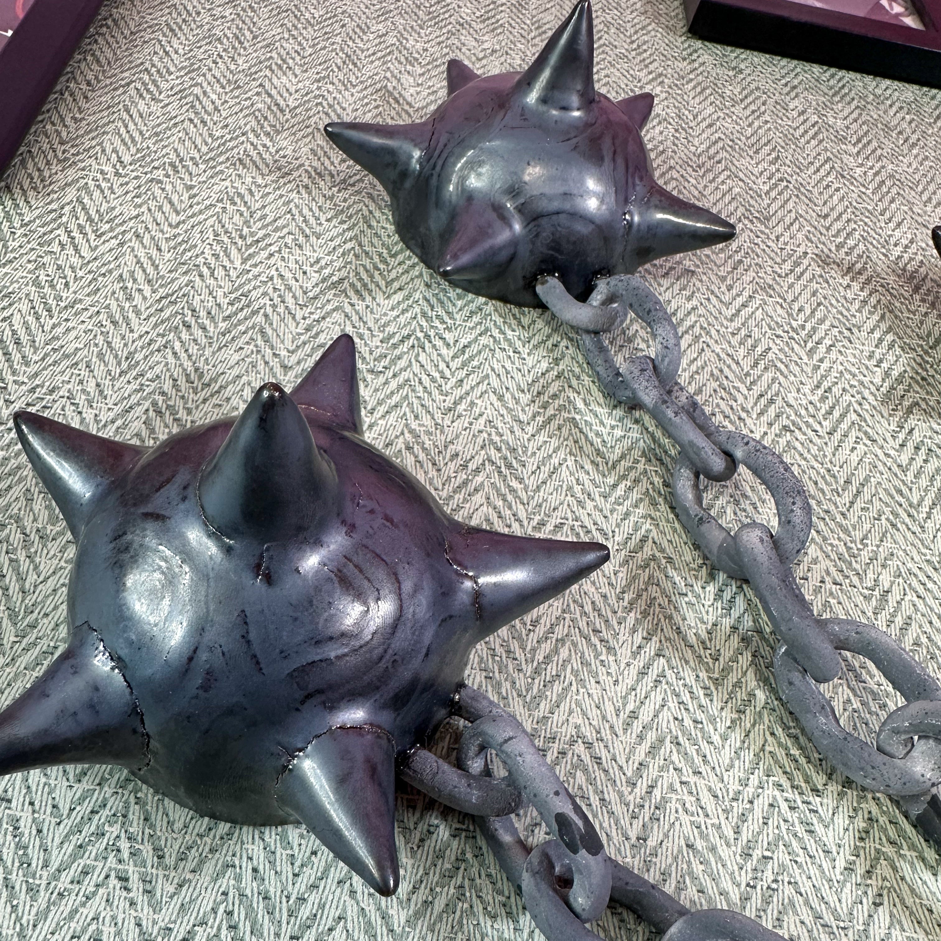 A close up of a ceramic sculpture of two spikey heads of a flail on chains